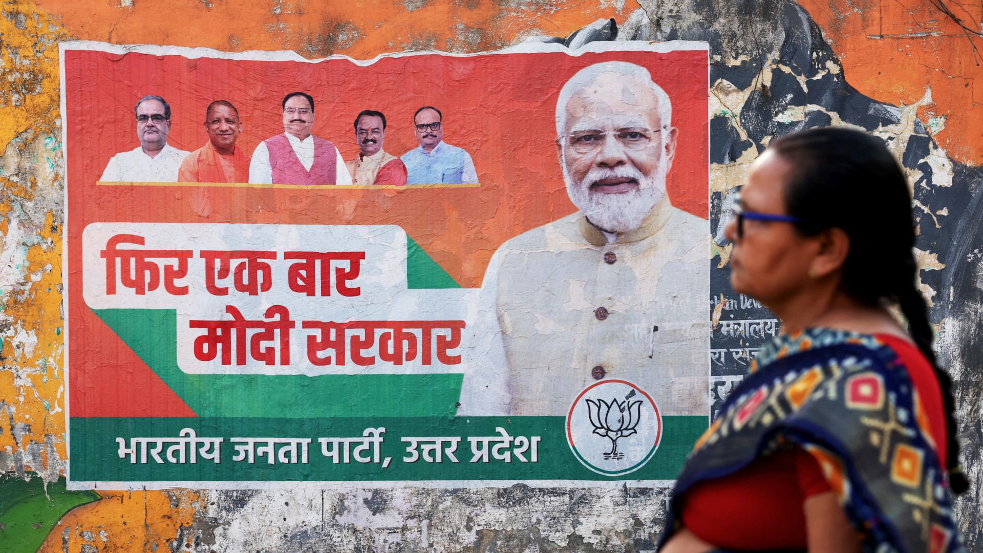 A woman walks past an election campaign poster of the Bharatiya Janata Party (BJP) featuring their leader and India's Prime Minister Narendra Modi, right, along a street in Varanasi on 24 March ahead of the country's upcoming general elections (Niharika Kulkarni/AFP)