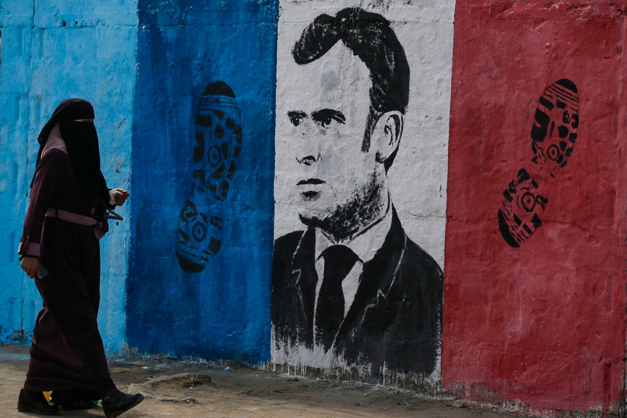 A Palestinian woman walks past a mural bearing the portrait French President Emmanuel Macron in Nuseirat refugee camp in the central Gaza Strip