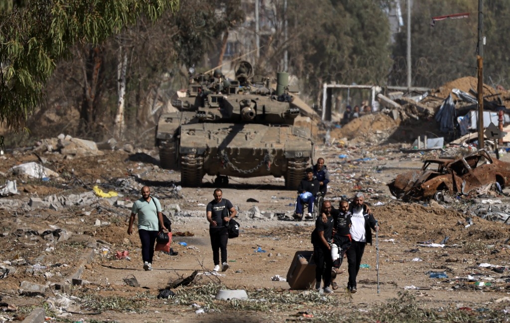 Palestinians fleeing the north through the Salaheddine road in the Zeitoun district on the southern outskirts of Gaza City, walk past Israeli army tanks on November 24, 2023