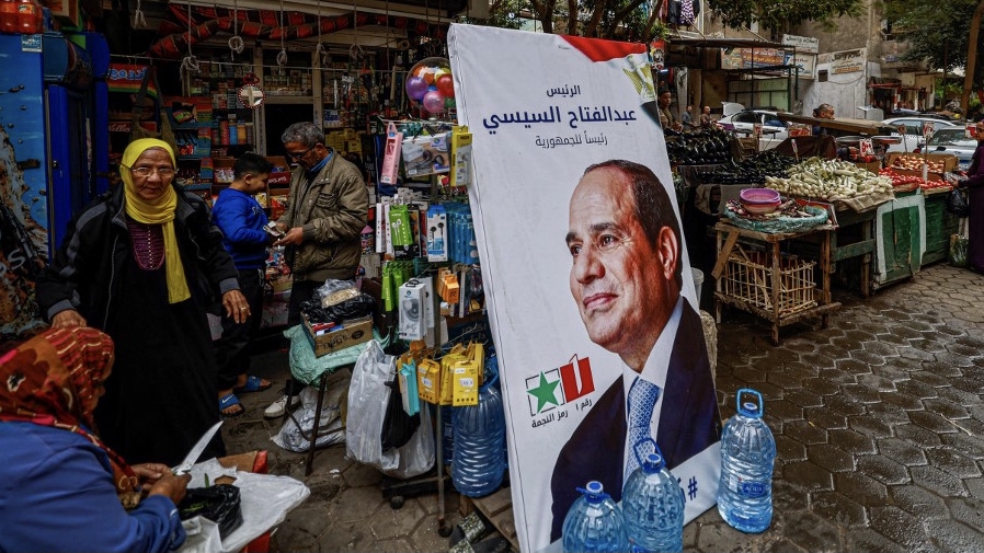 People walk past a campaign poster of Egypt's President Abdel Fattah el-Sisi in a market in Cairo on 7 December 2023, ahead of the presidential election (Khaled Desouki/AFP)