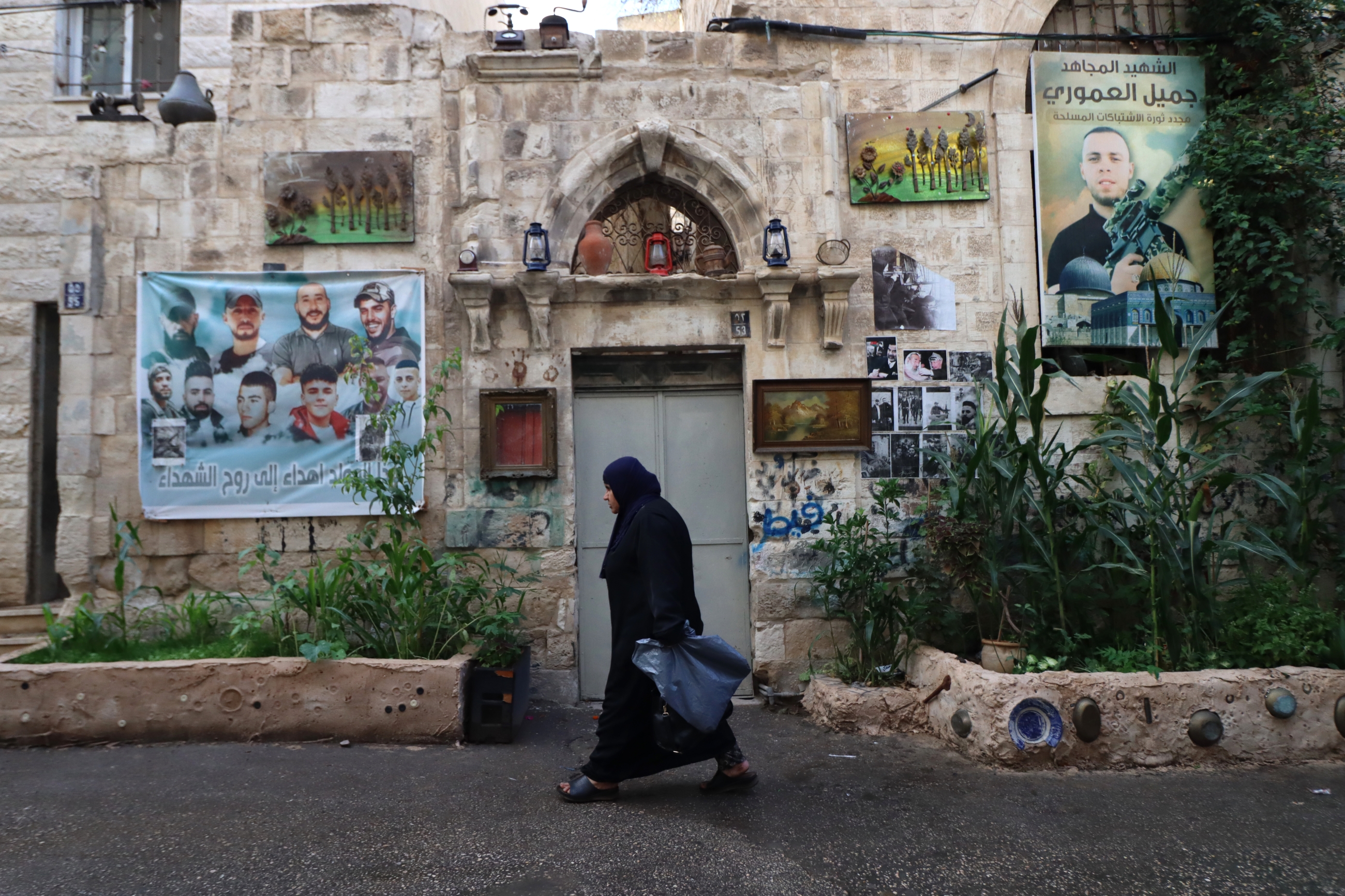 A Palestinian woman passes by photos of Nablus and Jenin fighters recently killed by the Israeli military, in Nablus' Old Town in the occupied West Bank on 9 November 2022 (MEE/Ahmad Al-Bazz)