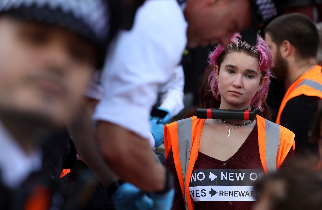 Protesters, with their necks padlocked together, block the road as they take part in a protest by Just Stop Oil climate activists at Piccadilly Circus, London, on 9 October 2022 (AFP)