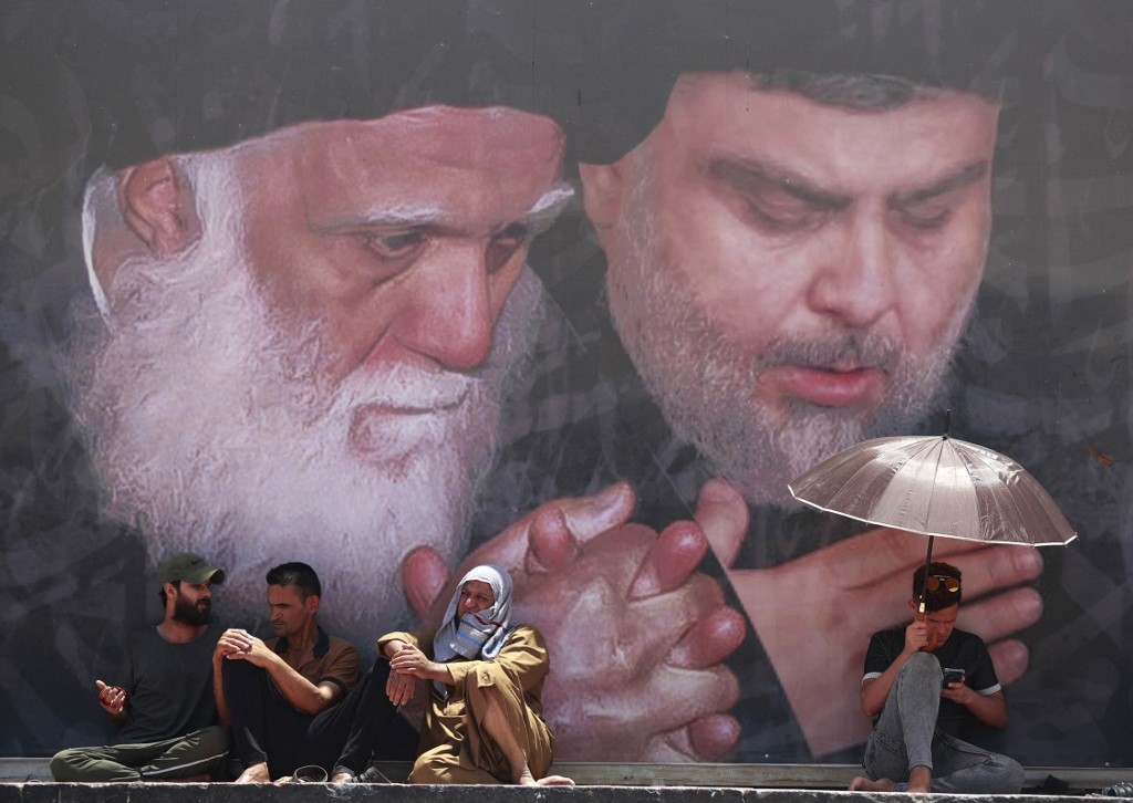 Des partisans de Moqtada al-Sadr assistent à la prière du vendredi sous une fresque représentant le leader chiite (à droite) à Sadr City, à l’est de Bagdad, le 17 juin 2022 (AFP)