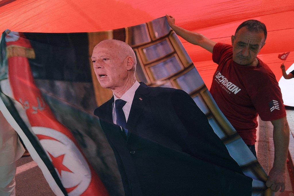 A supporter of President Kais Saied hold his image as he stands under a national flag during a rally in Tunis on 25 July (Fethi Belaid/AFP)