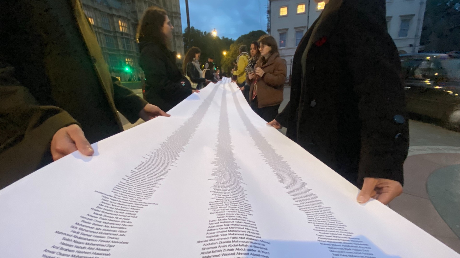 Two dozen attendees hold a 15-metre scroll with the names of all those killed in the 7 October attacks on Israel and the war on Gaza over the past year (Dania Akkad/Middle East Eye)