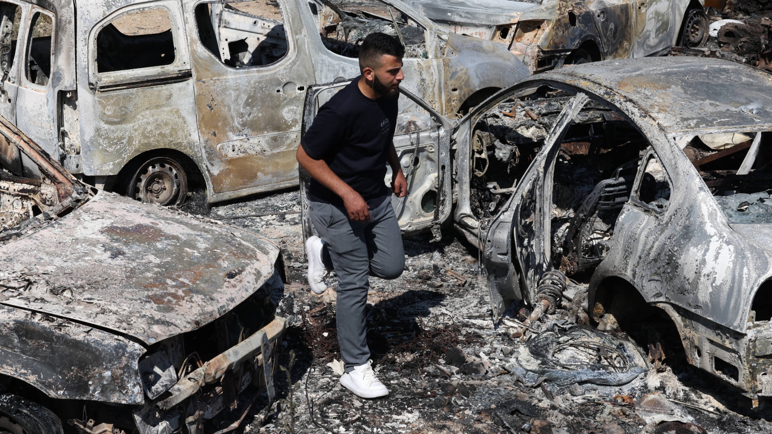 A man walks amidst burnt cars, which were set ablaze by Israeli settlers, in the area of in al-Lubban al-Sharqiya in the occupied West Bank on June 21, 2023.