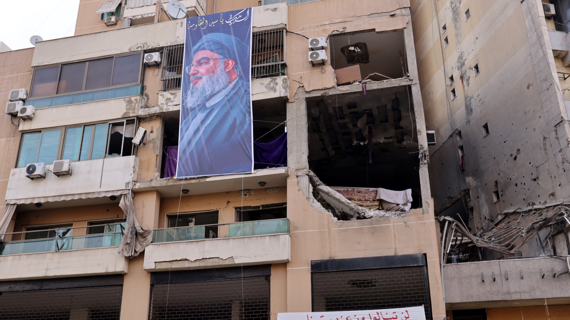 In a photo taken on 8 January, a banner depicting Hezbollah leader Hassan Nasrallah hangs on a building in which Hamas number two, Saleh al-Arouri, was assassinated in an Israeli drone strike in southern Beirut on 2 January (Anwar Amro/AFP)