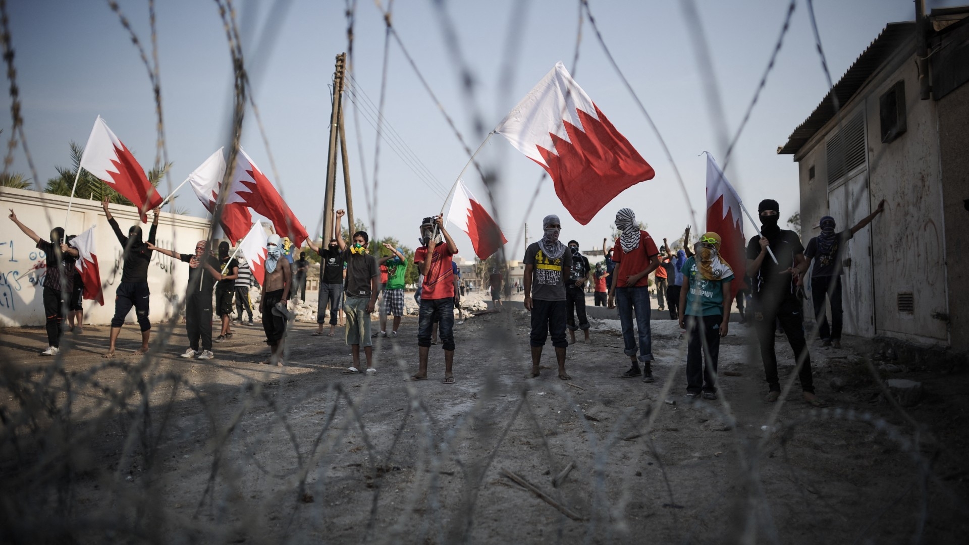 Bahraini protestors wave their national flag as they stand behind barbed wire placed by riot police in the village of Shakhora, west of Manama, on 14 August 2013 (AFP/Mohammed al-Shaikh)