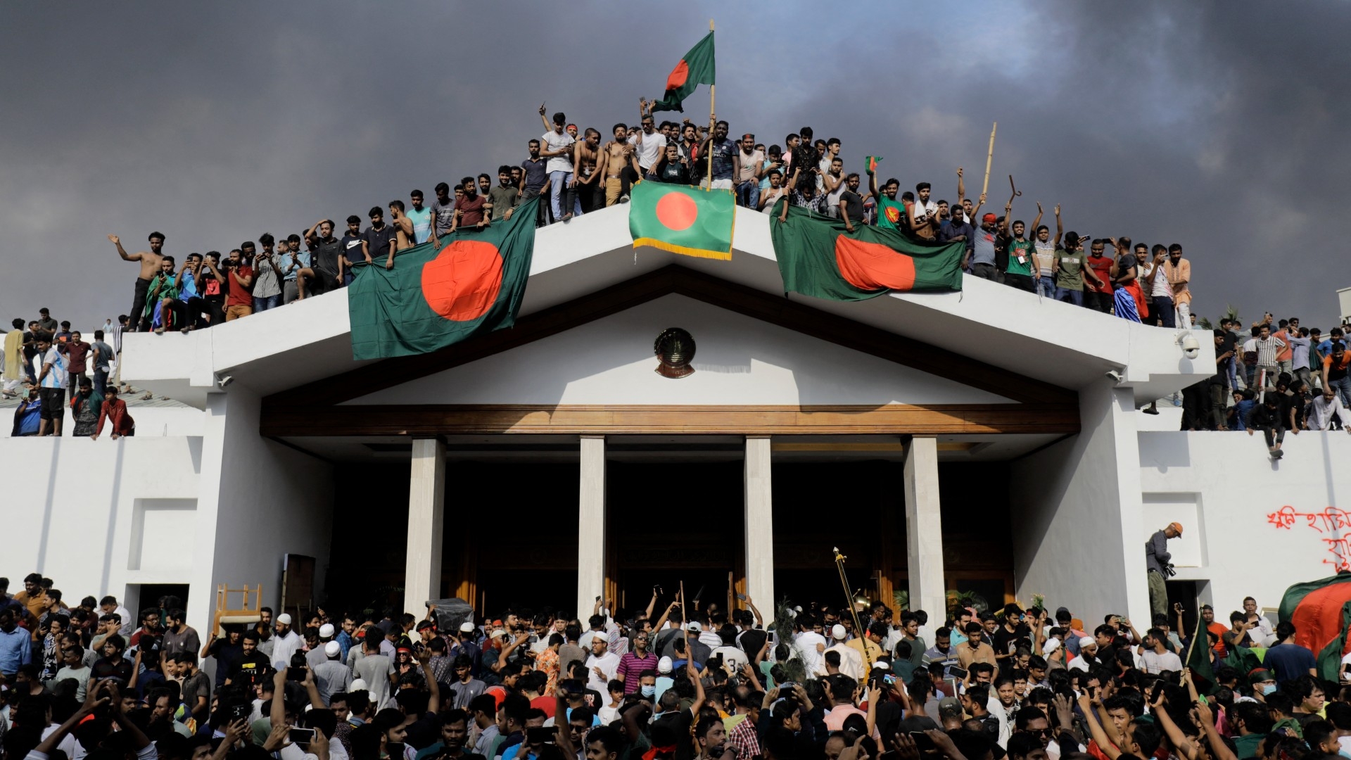 Anti-government protestors display Bangladesh's national flag as they storm Prime Minister Sheikh Hasina's palace in Dhaka on 5 August 2024 (AFP/K M Asad)