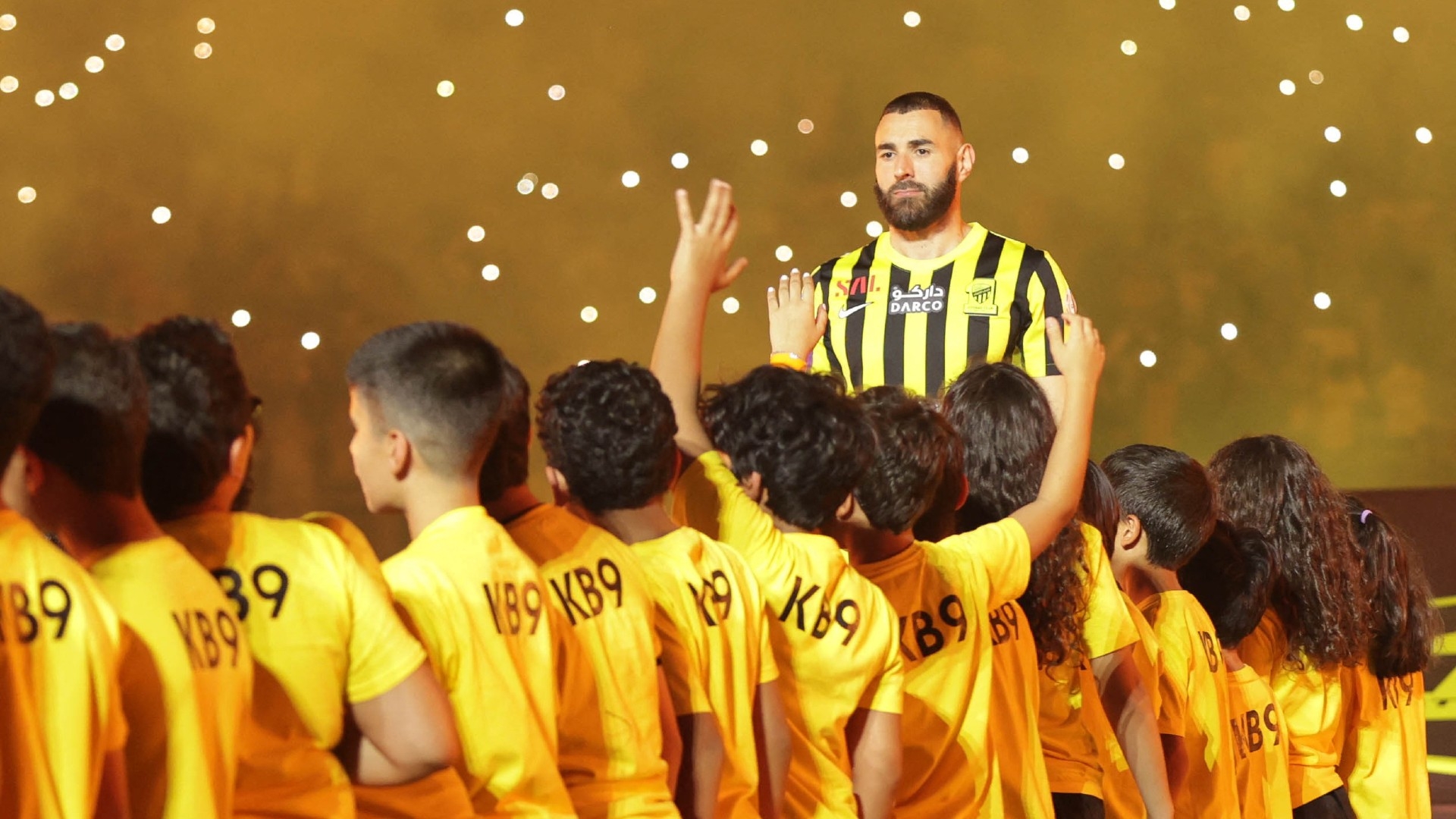 Karim Benzema, surrounded by children taking part in a ceremony, waves to the crowd at King Abdullah Sports City stadium in Jeddah, on 8 June 2023 (AFP)