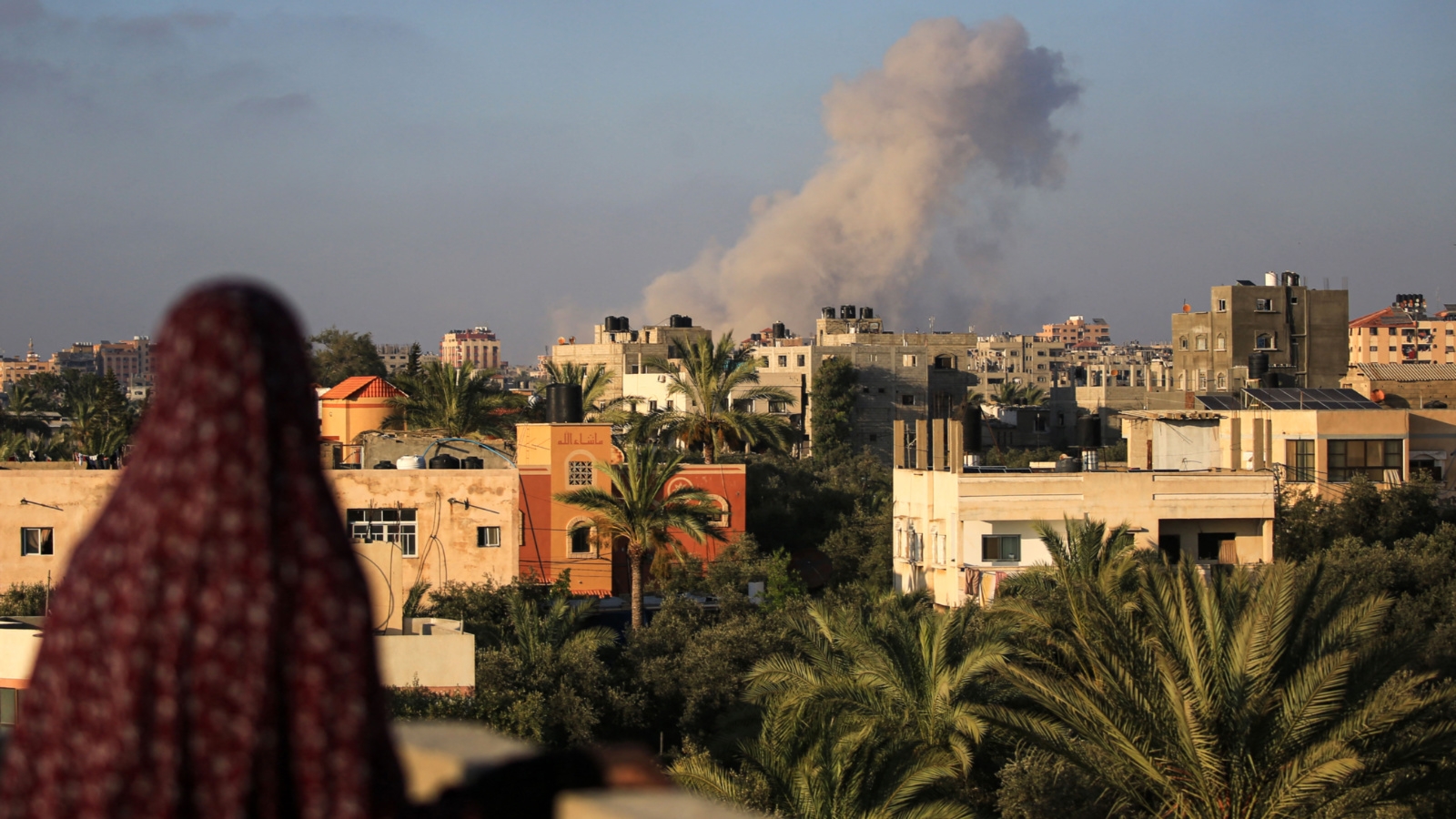 A Palestinian woman in al-Zawaida, central Gaza, watches the smoke rise following an Israeli air strike on the south on 11 June, 2024 (Eyad Baba/AFP)