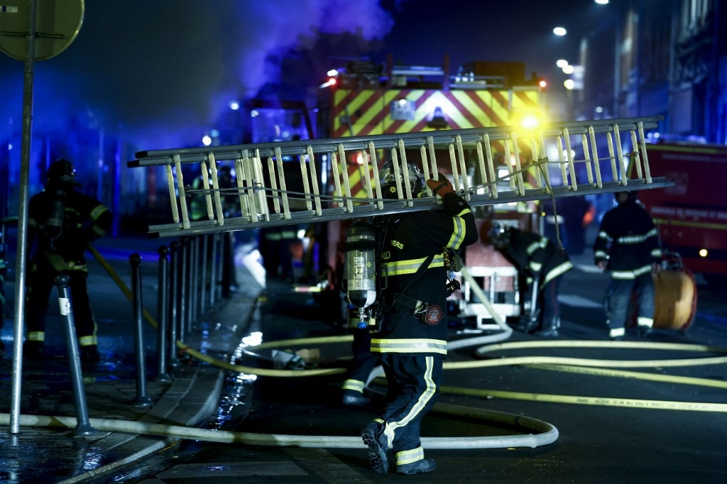 Des pompiers marchent avec du matériel après avoir éteint un incendie dans un hôtel lors de manifestations à Roubaix, dans le nord de la France, le 30 juin 2023 (AFP/Kenzo Tribouillard)