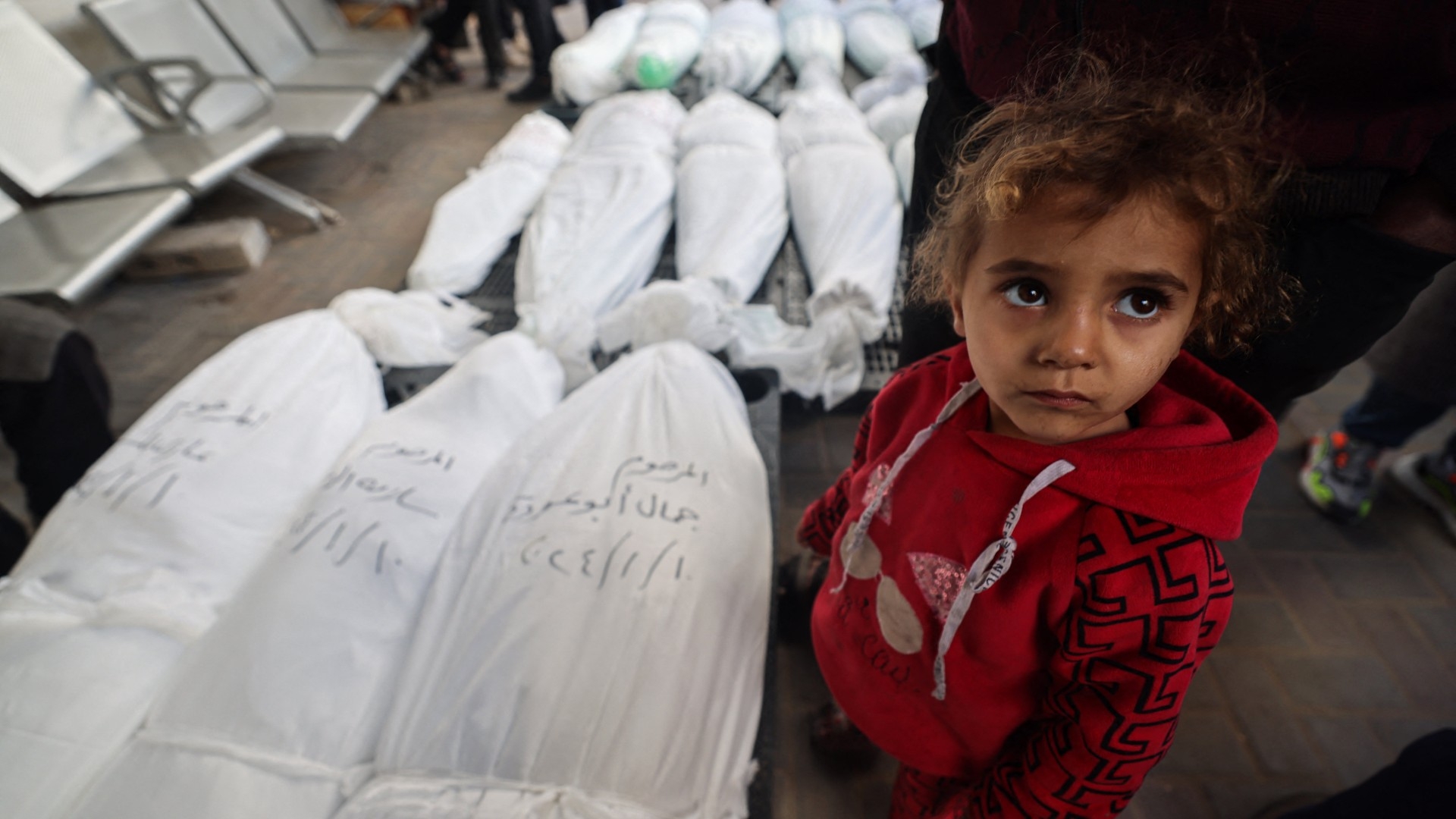 A child stands next to the bodies of family members after they were killed during Israeli bombardment, on 10 January in Rafah in the Gaza Strip (Mohammed Abed/AFP)