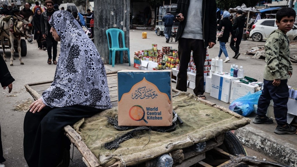 A Palestinian woman sits on a cart next to a box of food rations provided by US charity World Central Kitchen at a makeshift street market in Rafah in the southern Gaza Strip on 14 March (AFP)