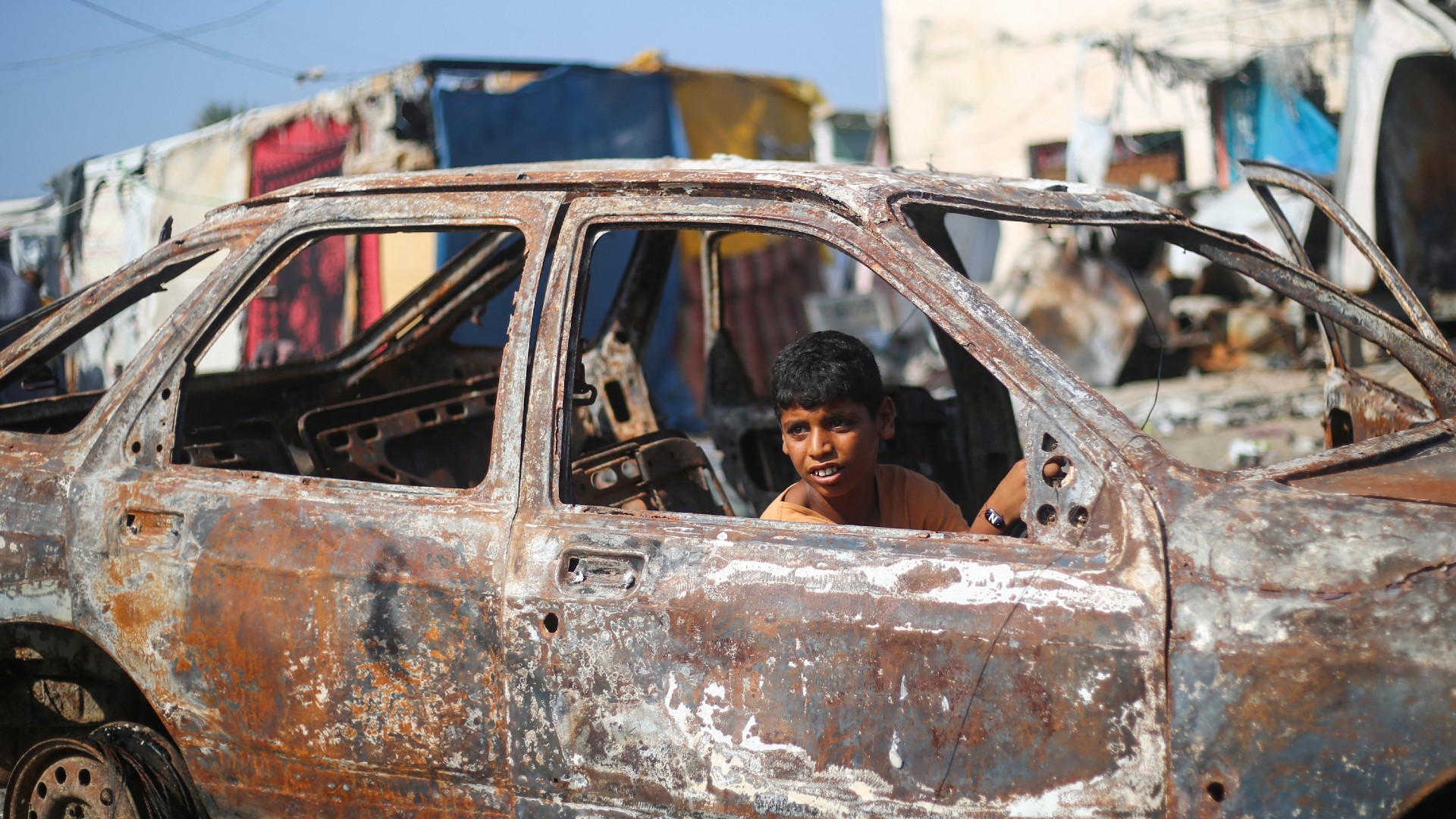 A boy plays in the wreckage of a car at the site of an Israeli air strike in the courtyard of al-Aqsa Martyrs Hospital in Deir al-Balah, central Gaza, on 16 October 2024 (AFP)