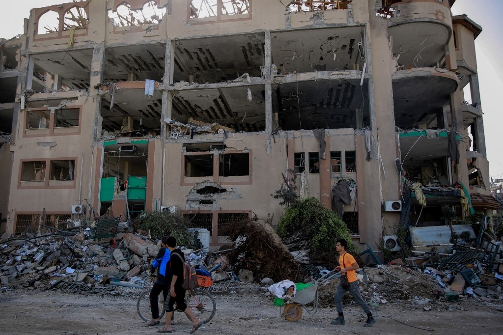 Palestinians walks past the destroyed building of the Islamic University in Gaza City on November 26, 2023, on the third day of a truce between Israel and Hamas (AFP)