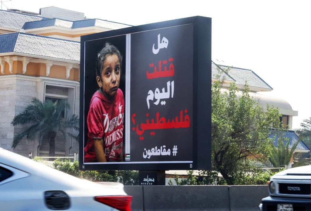 Des voitures passent devant un panneau publicitaire avec la photo d’un enfant palestinien et une inscription en arabe indiquant « Avez-vous tué un Palestinien aujourd’hui ? #boycott » à Koweït City le 26 octobre 2023 (AFP/Yasser al-Zayyat)