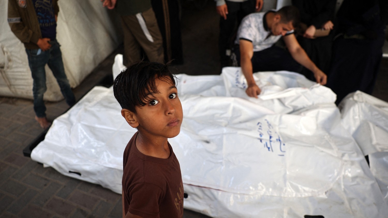 A young boy looks on as relatives of Palestinians killed in Israeli bombing mourn near their corpses in the yard of the Al-Najjar Hospital in Rafah in the southern Gaza Strip on 3 May 2024.