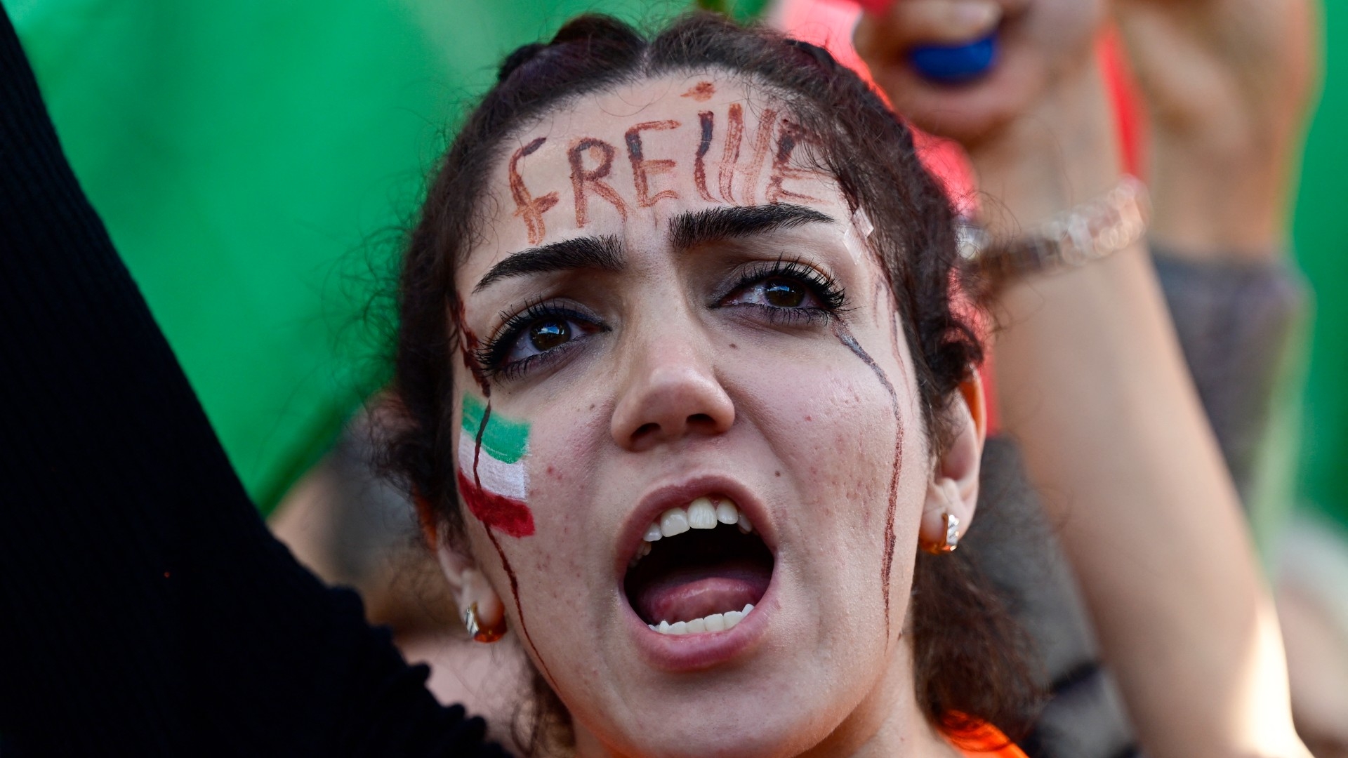 A protester with the word 'Freedom' written on her forehead and the Iranian flag painted on her cheek shouts slogans during a rally in support of the demonstrations in Iran, in Berlin on 22 October, 2022 (AFP)