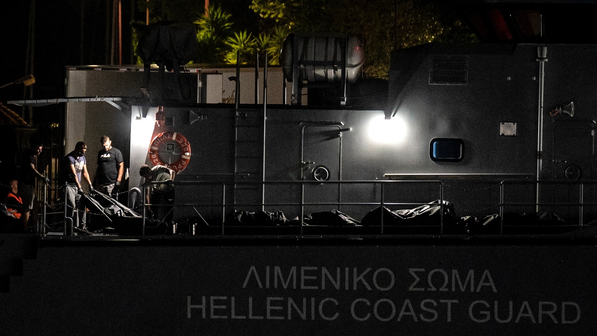Men carry bags with bodies from a coast guard vessel at the port in Kalamata, Greece on 14 June 2023 after a deadly shipwreck (AFP)