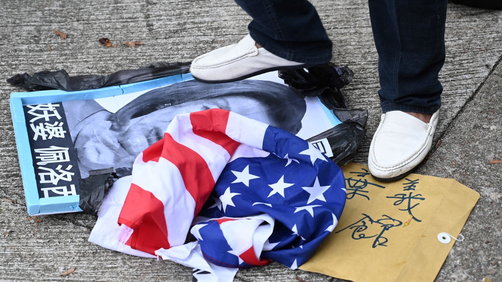 A pro-Beijing protester stamps on an image depicting the US House Speaker Nancy Pelosi and the US flag at a protest outside the US Consulate in Hong Kong on 3 August, 2022 (AFP)