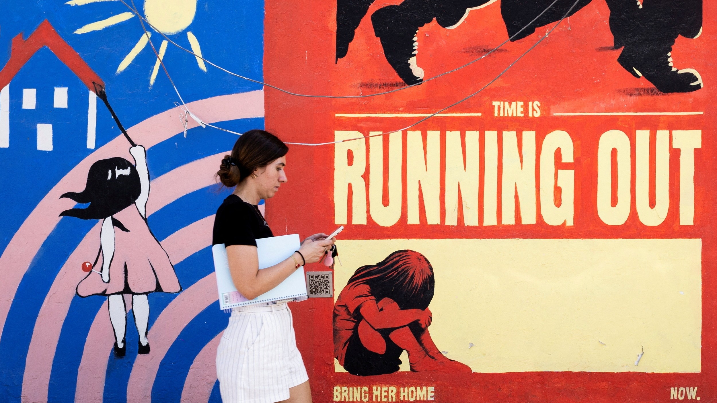 A woman walks past a mural in support of captives taken during the 7 October attack, in Tel Aviv, Israel, 9 July (Reuters/Eloisa Lopez)