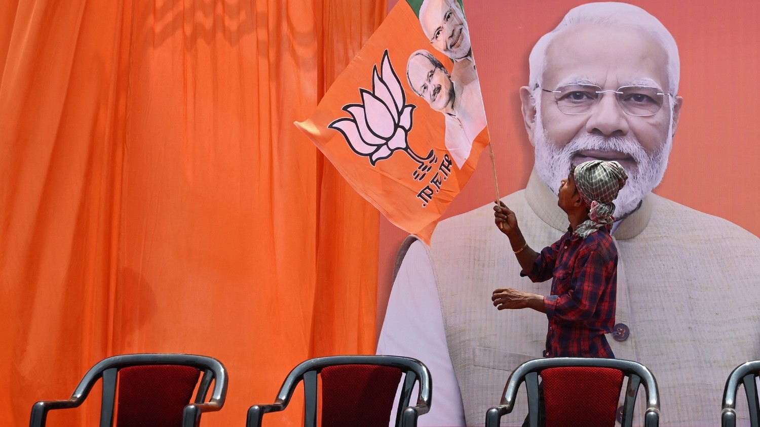 A worker fixes a flag of the ruling Bharatiya Janata Party (BJP) on a hoarding of their leader and India's Prime Minister Narendra Modi in Raipur on 15 April 2024.