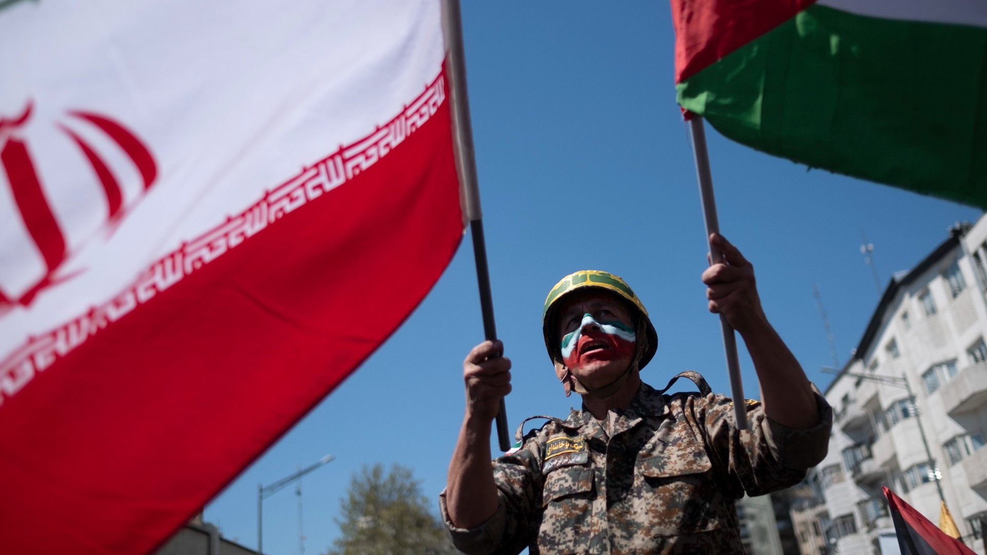 A protester wearing military uniform waves an Iranian and a Palestinian flag during a rally following the Damascus consulate strike, on 5 April (Reuters/Morteza Nikoubazl/NurPhoto)