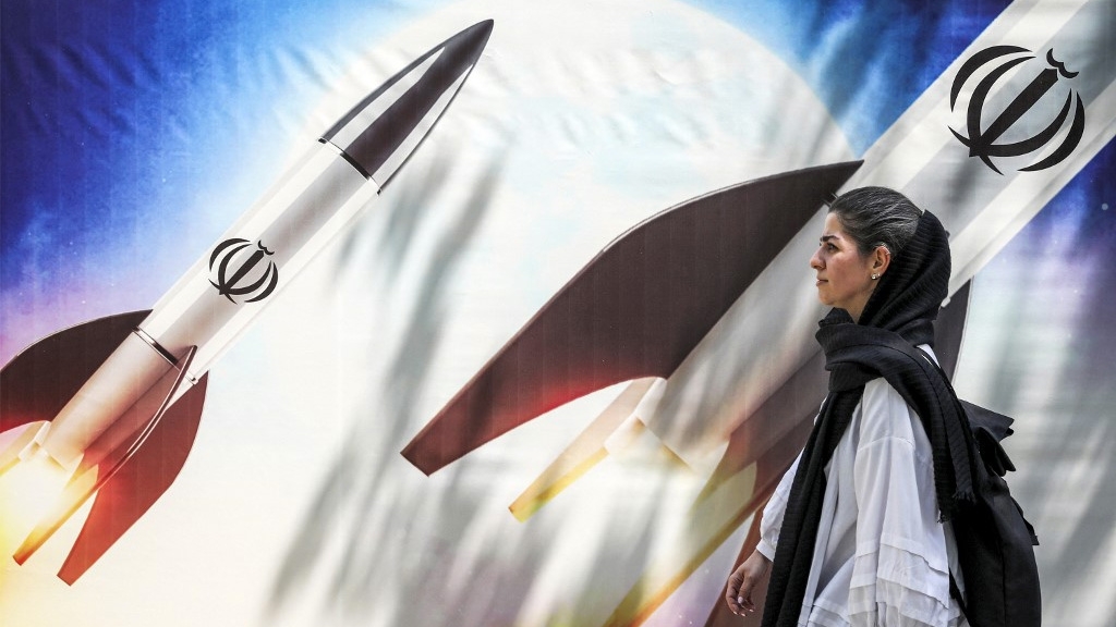 A woman walks by a banner depicting a missile launch in Tehran on 15 April 2024 (Atta Kenare/AFP)