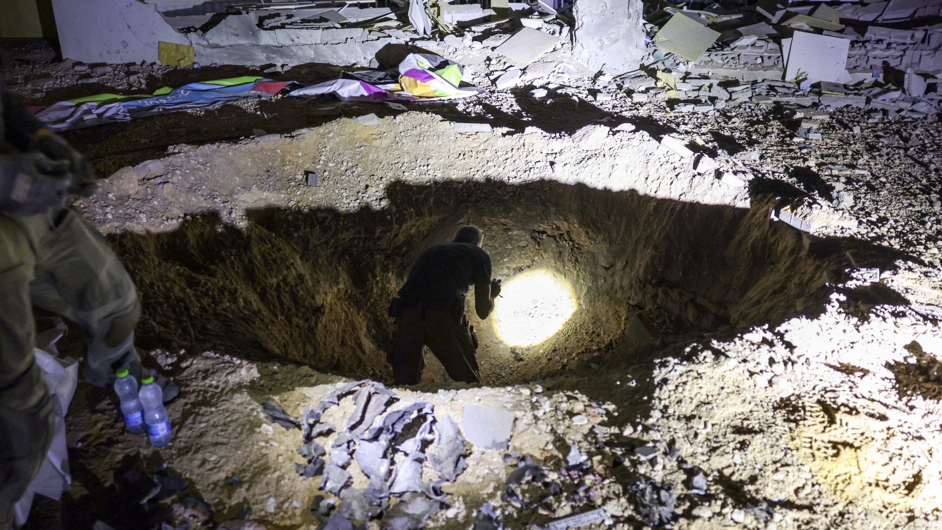 Members of Israel's Home Front Command and police forces inspect a crater left by an Iranian missile in the southern city of Gedera on 1 October 2024 (AFP)