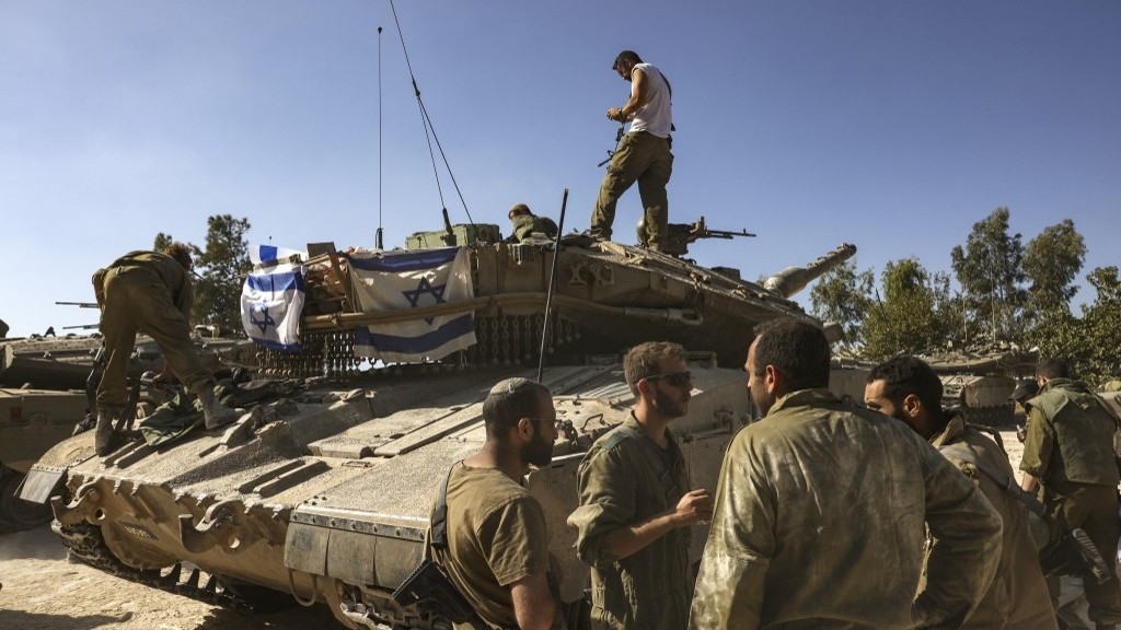 Israeli soldiers gather near their Merkava tank stationed outside Kibbutz Beeri near the border with the Gaza Strip on 20 October 2023 (AFP)