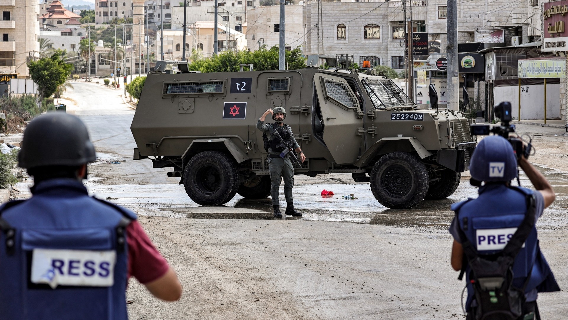 Journalists film near Israeli army armoured vehicles deployed at the entrance of the Tulkarm refugee camp in the occupied West Bank on 22 August 2024 (AFP/Zain Jaafar)