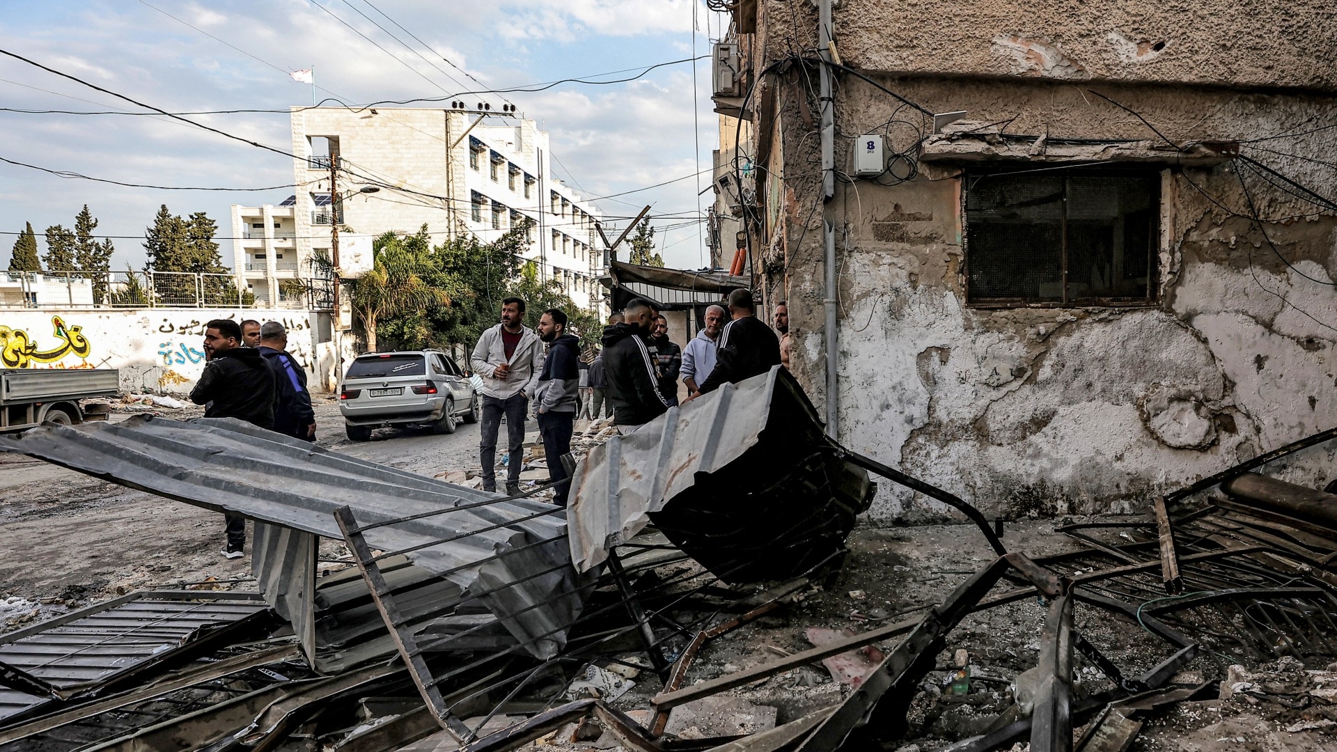 Palestinian men stand by debris outside a damaged building in the aftermath of an Israeli raid in the Nur Shams refugee camp near the northern city of Tulkarm in the occupied West Bank on 27 December 2023 (AFP)