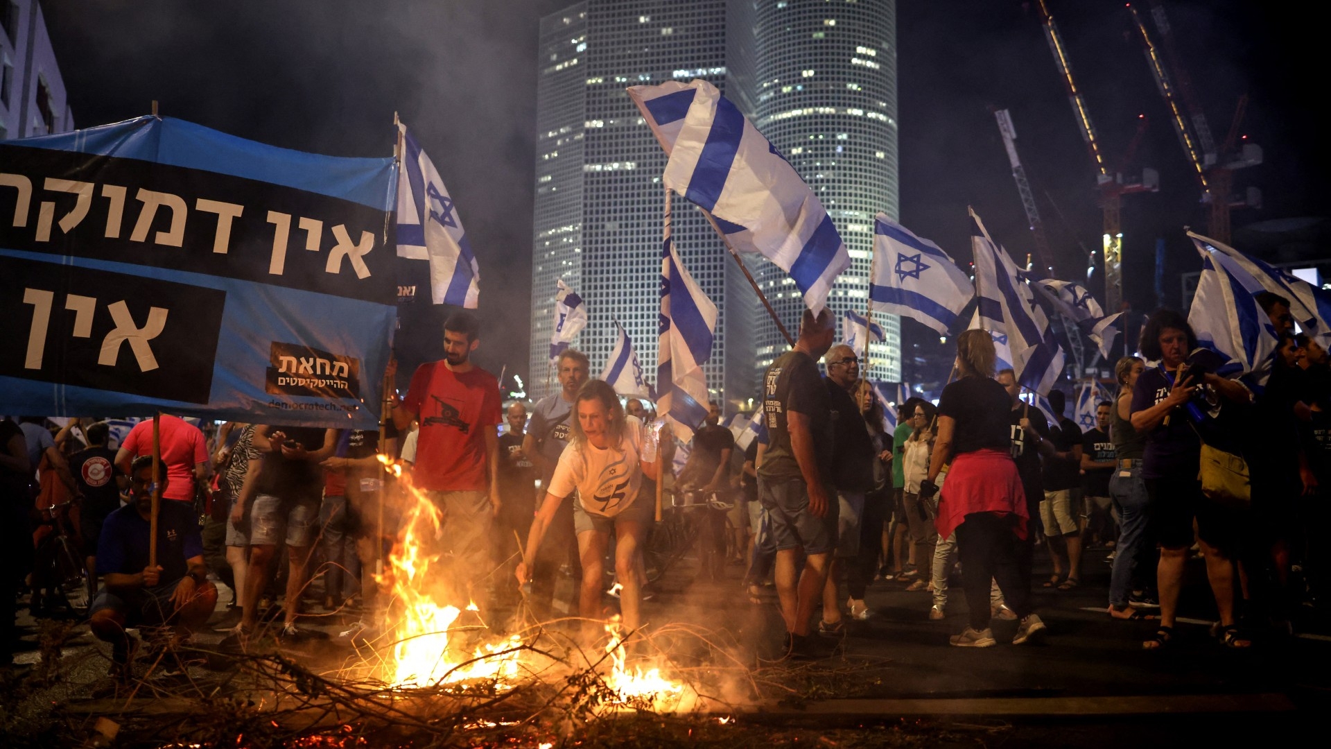 Anti-government protesters raise flags and light a fire on Ayalon Highway in Tel Aviv on 5 July 2023 (AFP)
