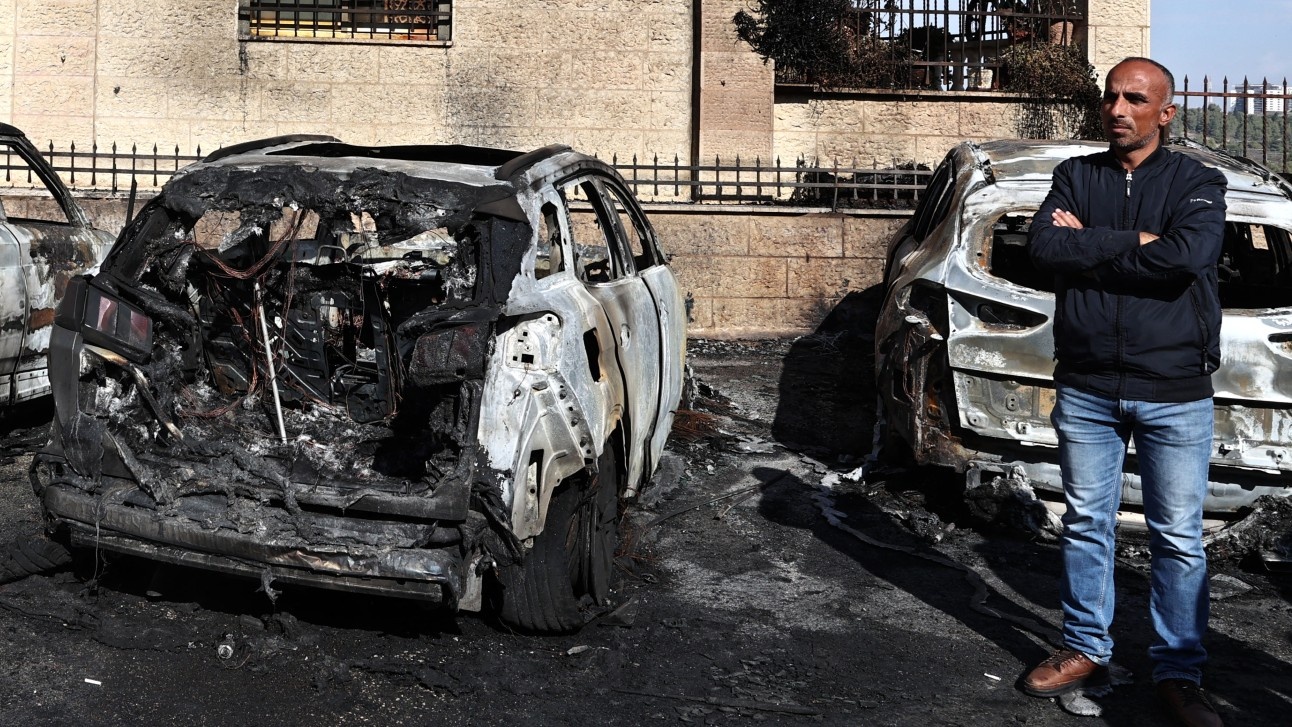 A man stands by burnt vehicles at the site of a reported attack by Israeli settlers in a residential area on the outskirts of Ramallah city in the occupied West Bank, on 4 November 2024.