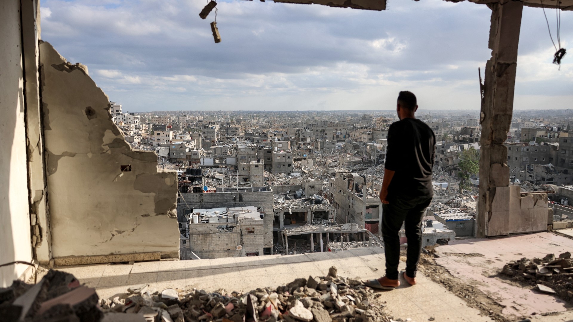 A man standing atop a heavily damaged building views other destroyed buildings in Khan Younis in the southern Gaza Strip on 7 October 2024  (AFP/Bashar Taleb)