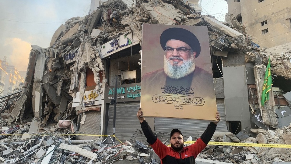 A man flashes a portrait of slain Hezbollah chief Hassan Nasrallah at the site of an Israeli air strike in Beirut’s southern suburbs on 12 November 2024 (AFP)