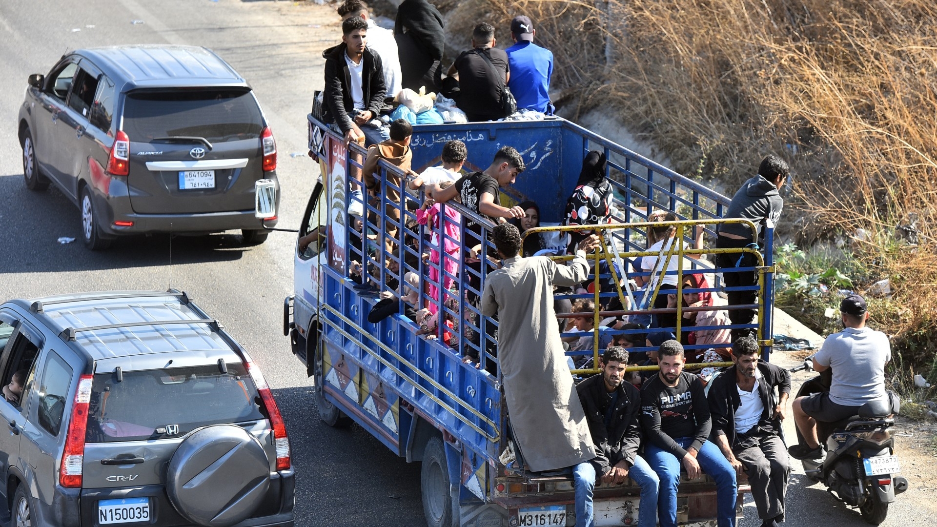 People sit with their belongings in the back of a truck as they arrive in the coastal town of Naameh, south of Lebanon's capital Beirut, on 24 September 2024 (Fadel Itani/AFP)