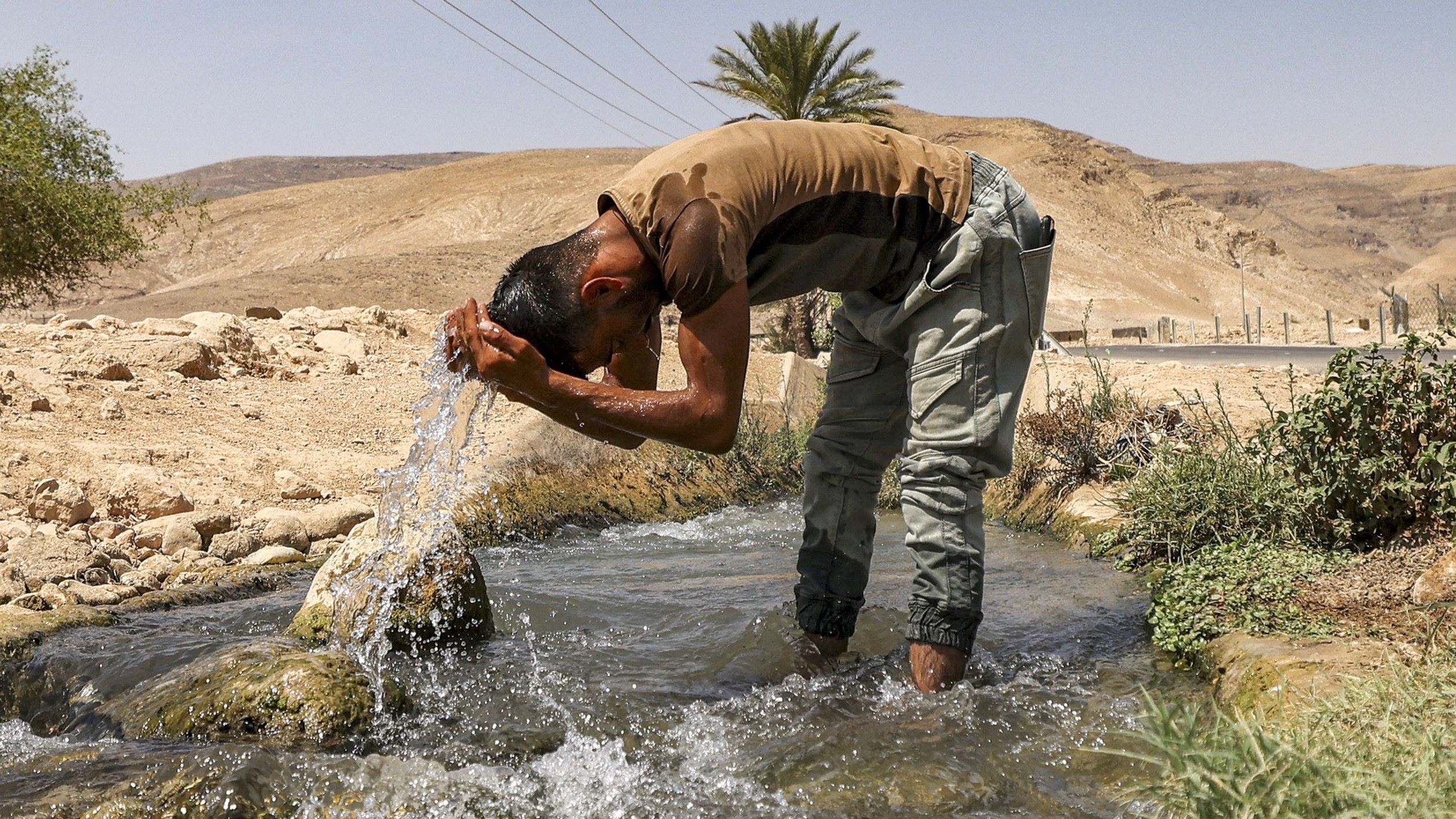 Un homme se rafraîchit près d’un ruisseau au nord de la ville palestinienne de Jéricho (AFP/Hazem Bader)