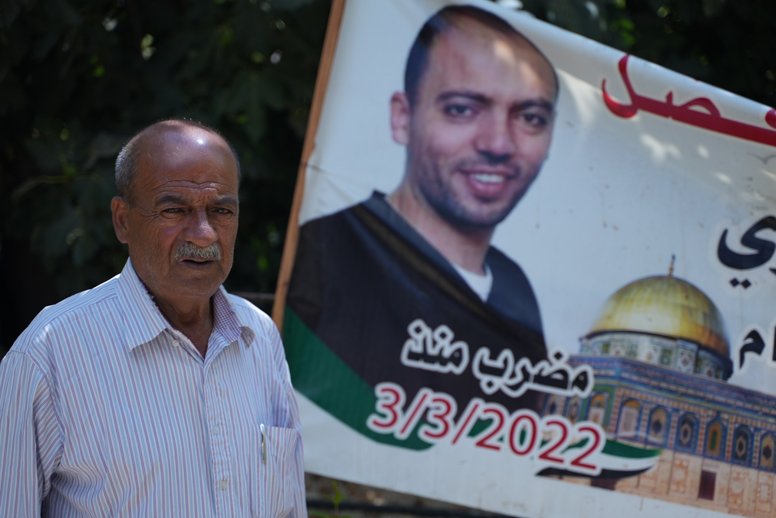Mohammed Awawdeh poses for a picture in his home in Hebron, with a poster of his detained son Khalil Awawdeh, who is on his 173rd day of hunger strike in an Israeli prison (MEE)