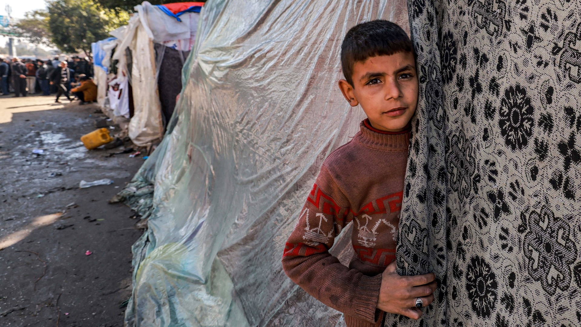A child peeks out of a tent sheltering displaced Palestinians in Rafah in the southern Gaza Strip on 8 February 2024 (AFP)