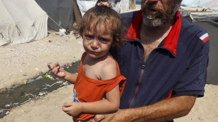 A man holds a child at a makeshift camp for displaced Palestinians in Deir al-Balah, in the central Gaza Strip, on 19 August 2024 (Eyad Baba/AFP)