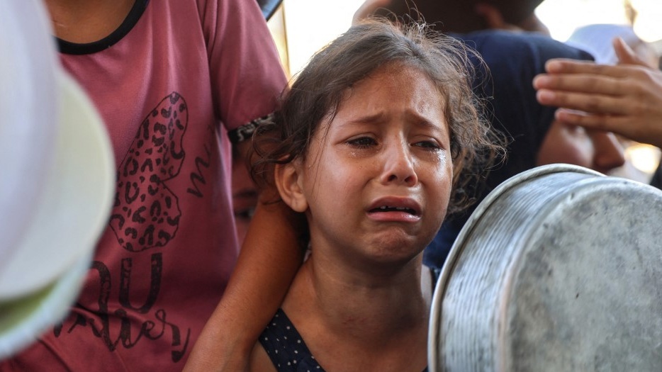 A displaced Palestinian child cries as she lines up with others to receive food aid in Beit Lahia, northern Gaza, on 18 July 2024 (Omar al-Qattaa/AFP)