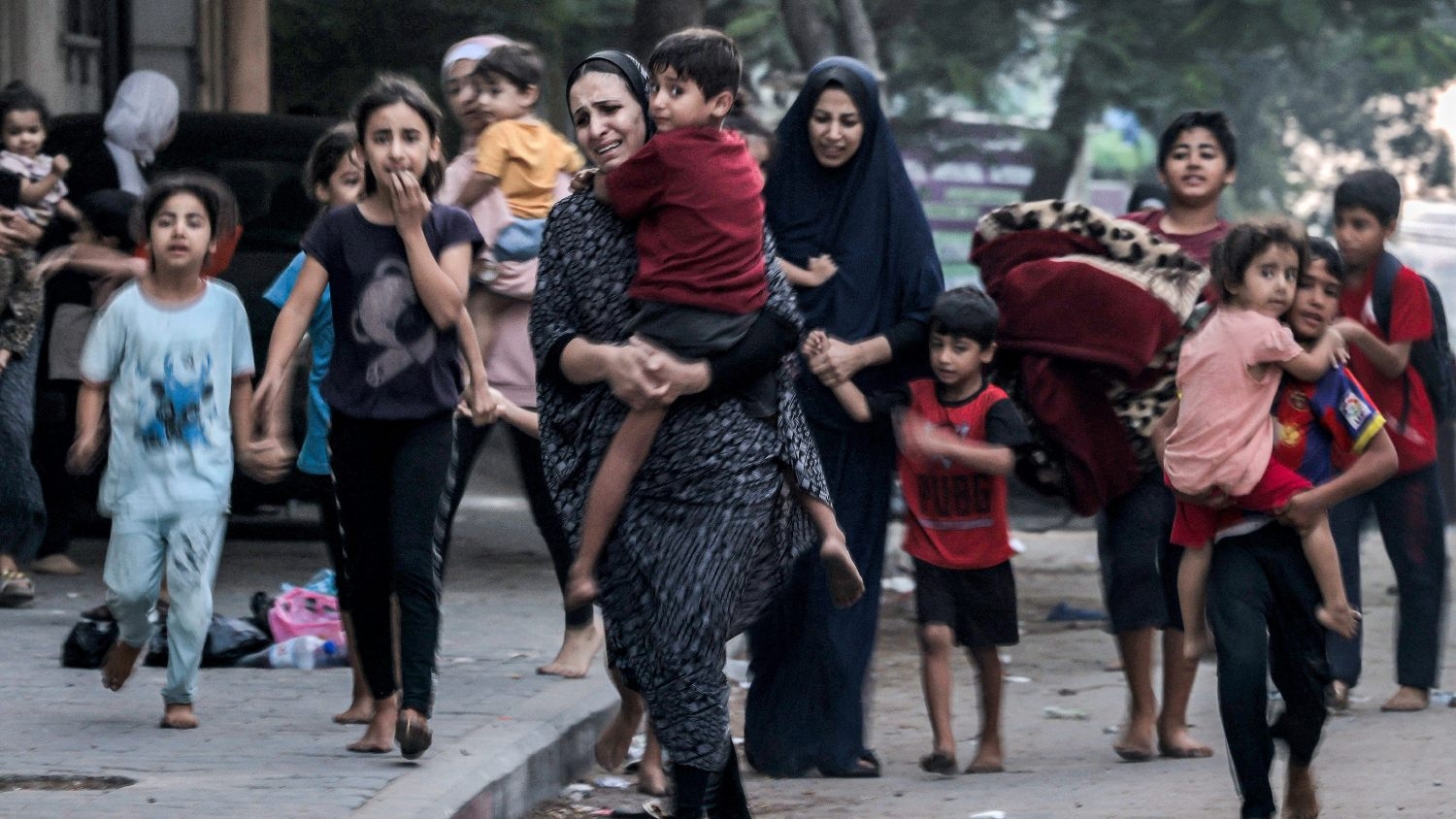 Palestinian women with their children fleeing from their homes following Israeli air strikes rush along a street in Gaza City on 11 October 2023.