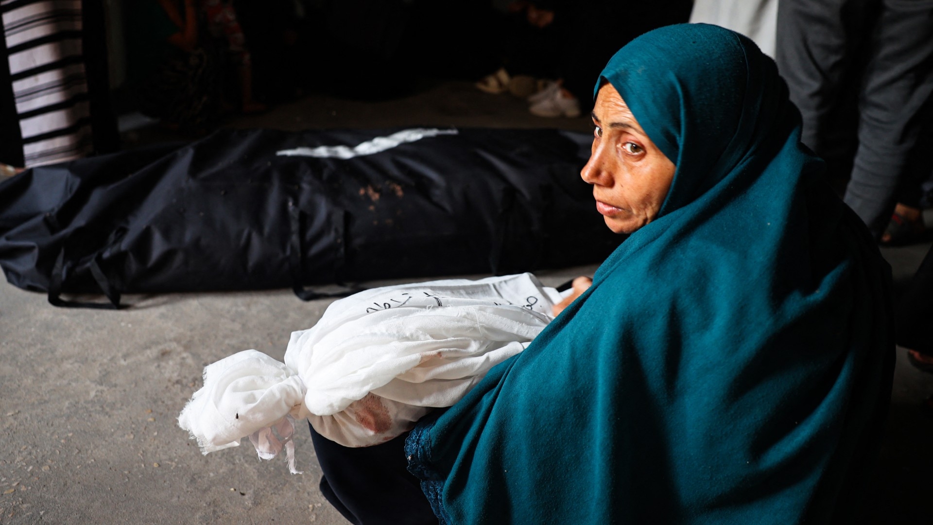 A Palestinian woman holds the shrouded body of a child killed in Israeli bombardment in Rafah, southern Gaza Strip, on 26 May 2024 (Eyad Baba/AFP)