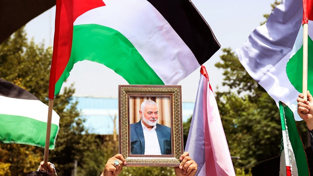 People hold up the Palestinian flag and a portrait of assassinated Hamas political chief Ismail Haniyeh during a rally in Tehran on 31 July 2024 (AFP)