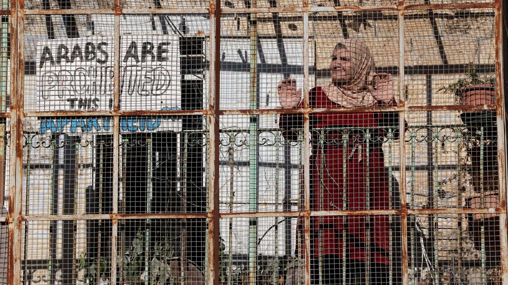 A Palestinian woman stands at the fence of her house in al-Shuhada street, which is largely closed to Palestinians, in Hebron on 9 November 2021.