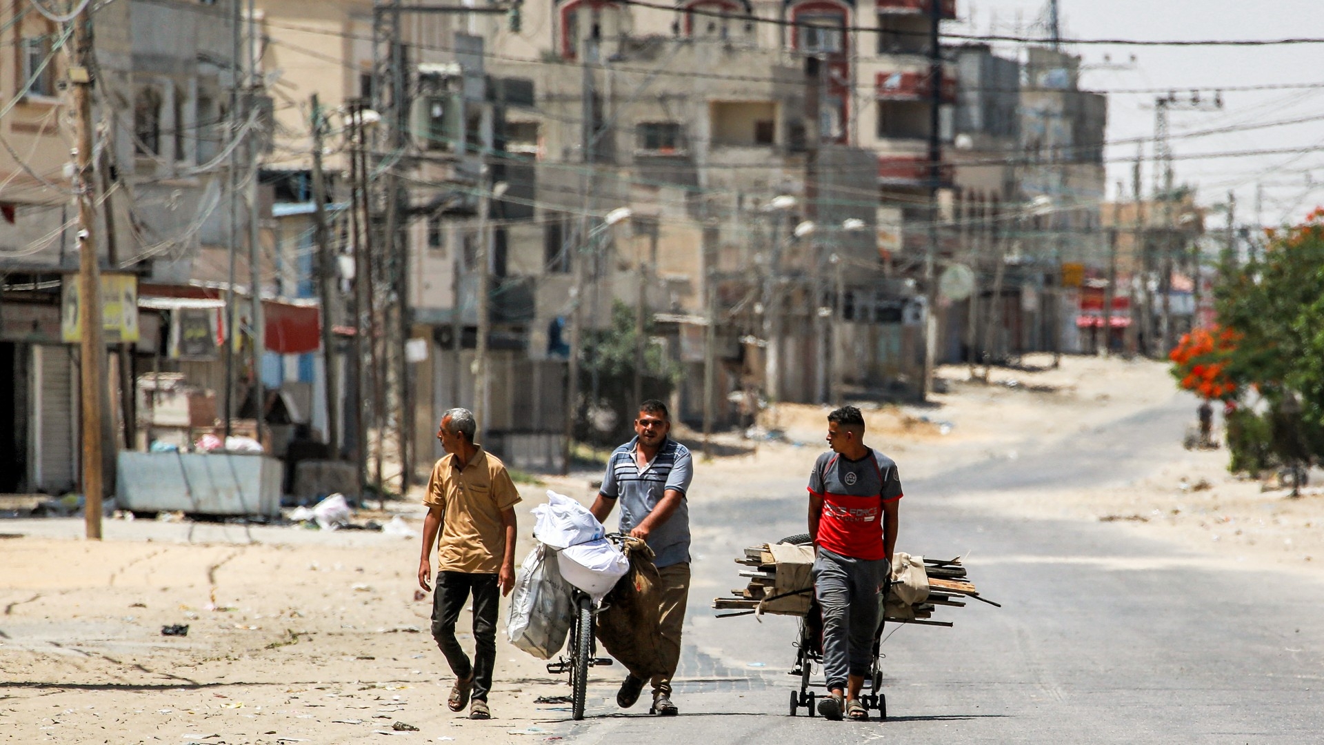A man pulls a cart while another pushes a bicycle loaded with bags along a street in the eastern part of Rafah in the southern Gaza Strip on 14 June 2024 (AFP/Bashar Taleb)