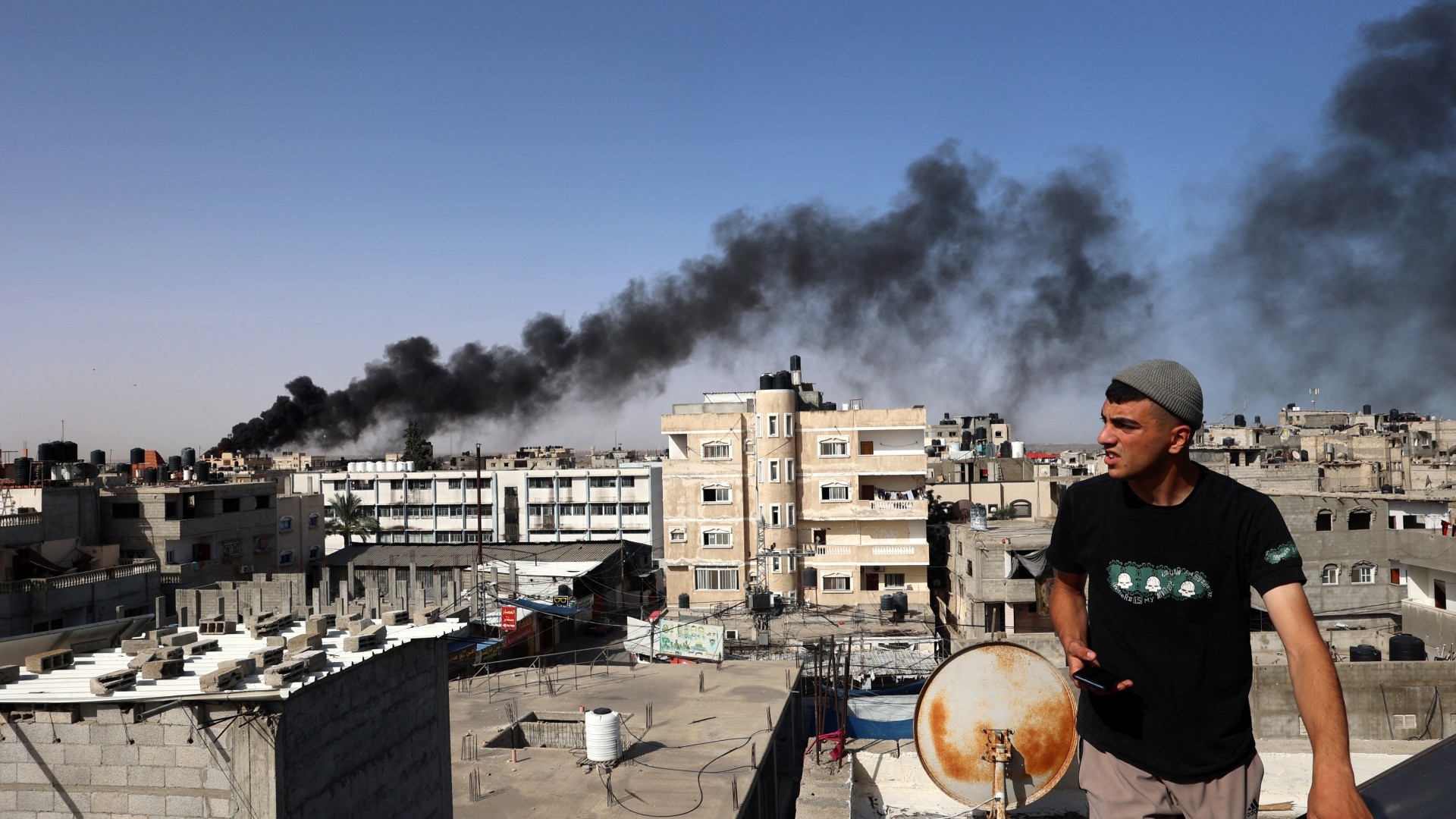 A man looks on as thick, black smoke rises from a fire in a building caused by Israeli bombardment in Rafah on 10 May 2024 (AFP)