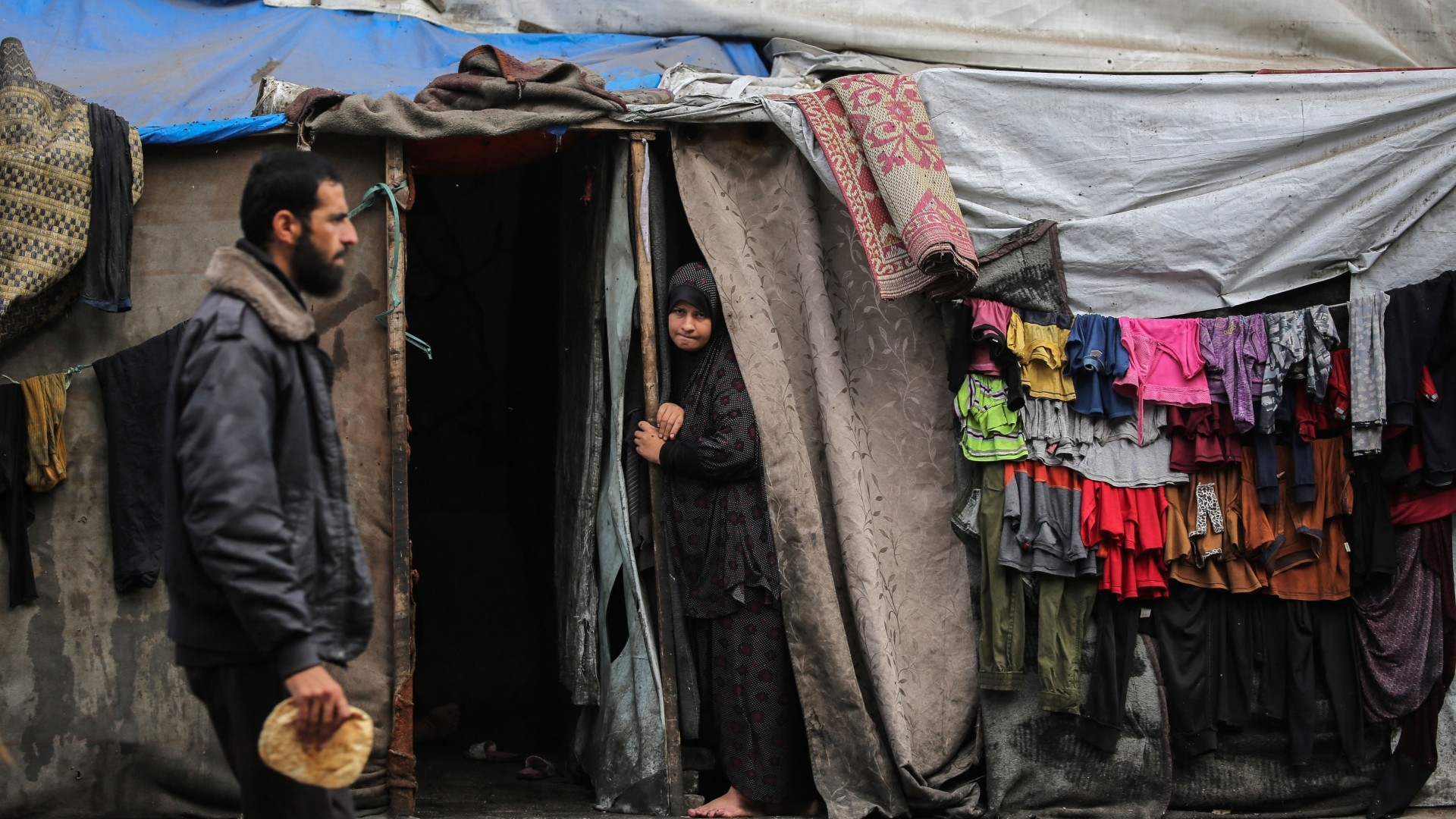 A Palestinian man walks past as a woman stands at the entrance of a tent in an area housing displaced people in Rafah on 30 April (AFP)